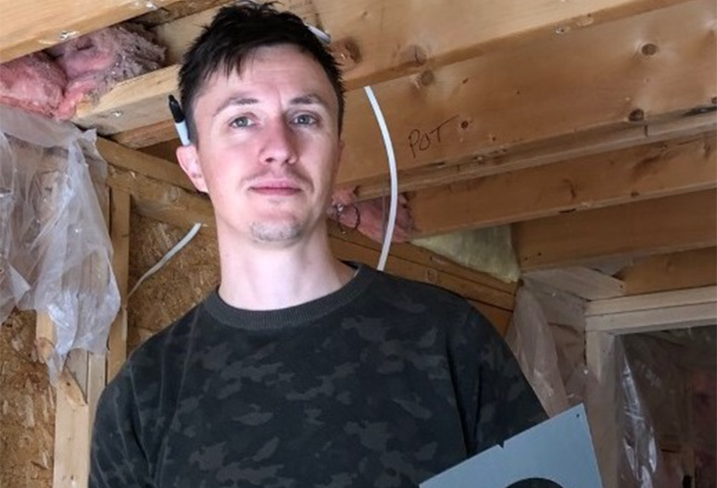 A man is standing in a wooden room holding a piece of paper.