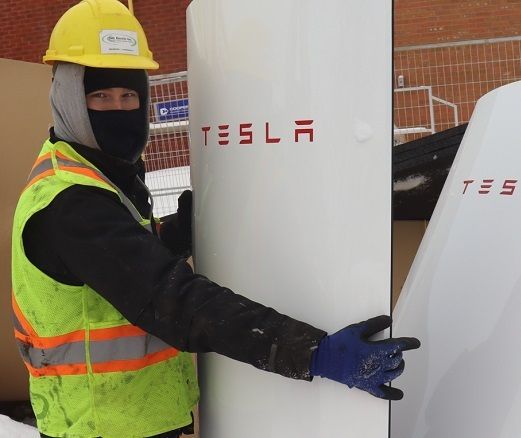 A man wearing a yellow hard hat is holding a tesla sign