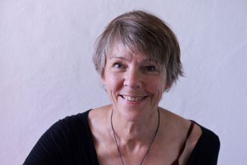 Eine Frau in schwarzer Jacke und lila Rollkragenpullover lächelt in die Kamera