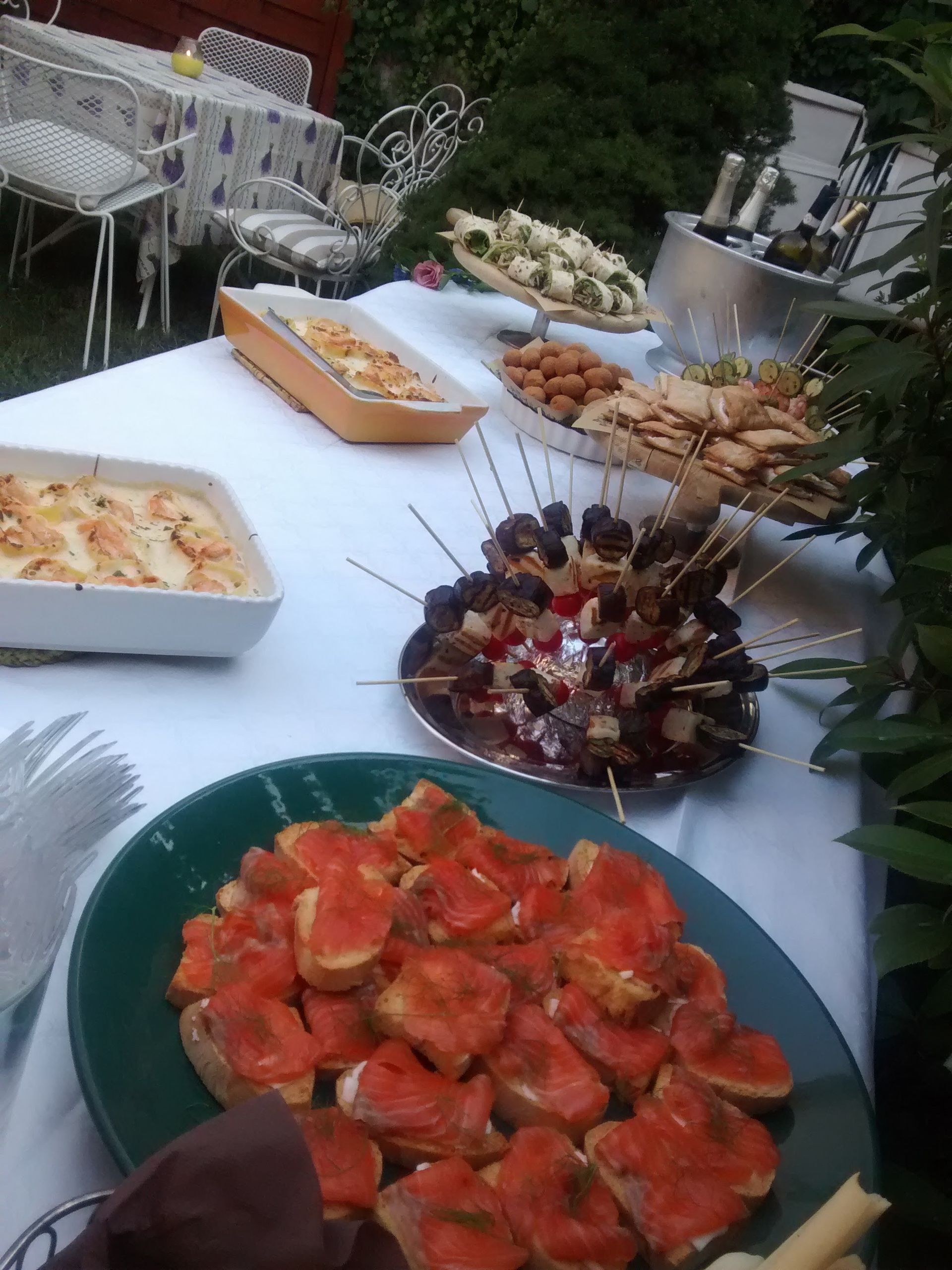 Tavolo da buffet con pomodori rossi a fette, spiedini di antipasti e vassoi di cibo in un ambiente all'aperto.