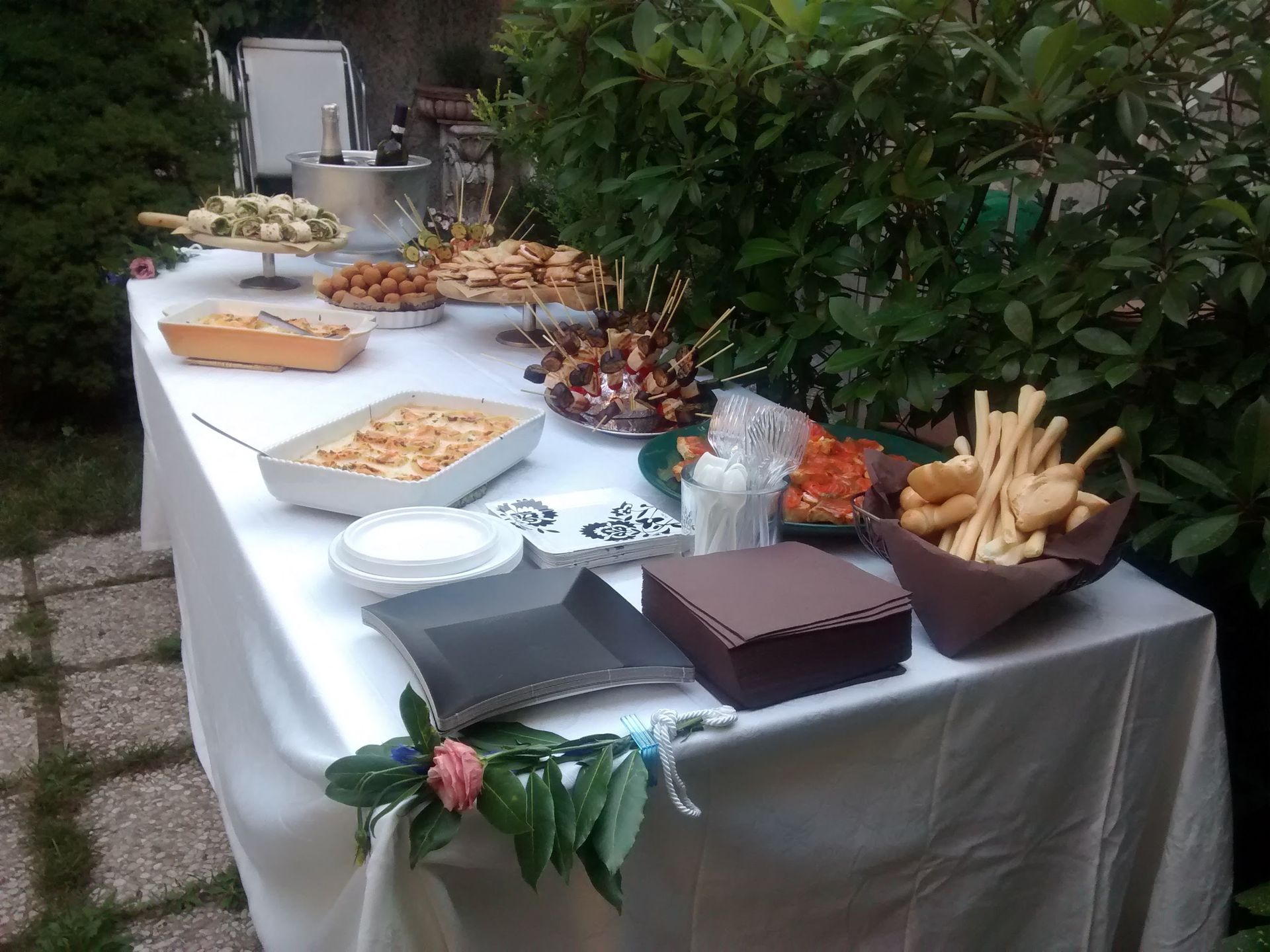 Tavolo da buffet all'aperto con tovaglia bianca, assortimento di antipasti, grissini e pasticcini.