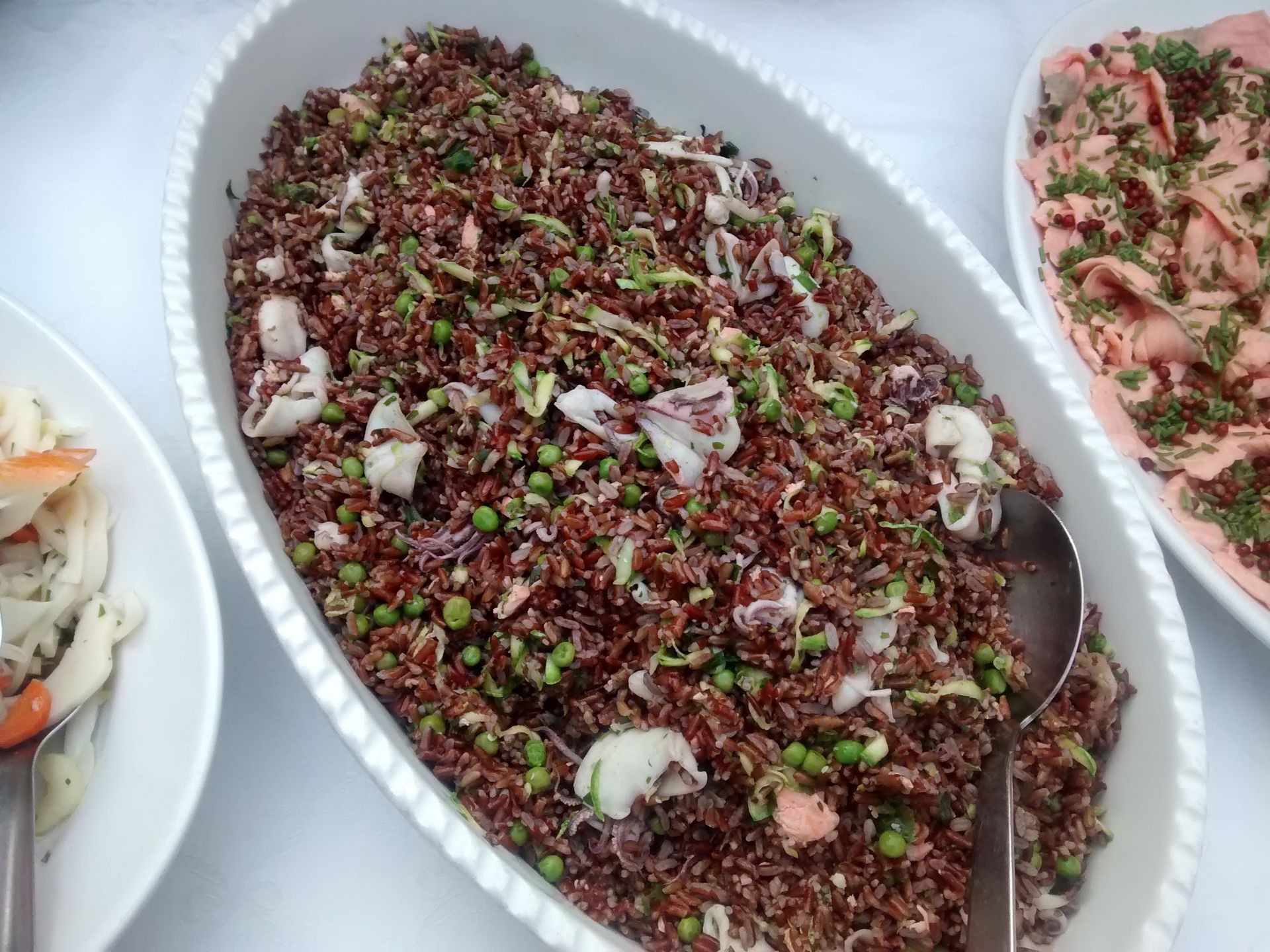 Tre vassoi di insalate miste con erbe aromatiche e frutti di mare, tra cui un'insalata di cereali scuri al centro.