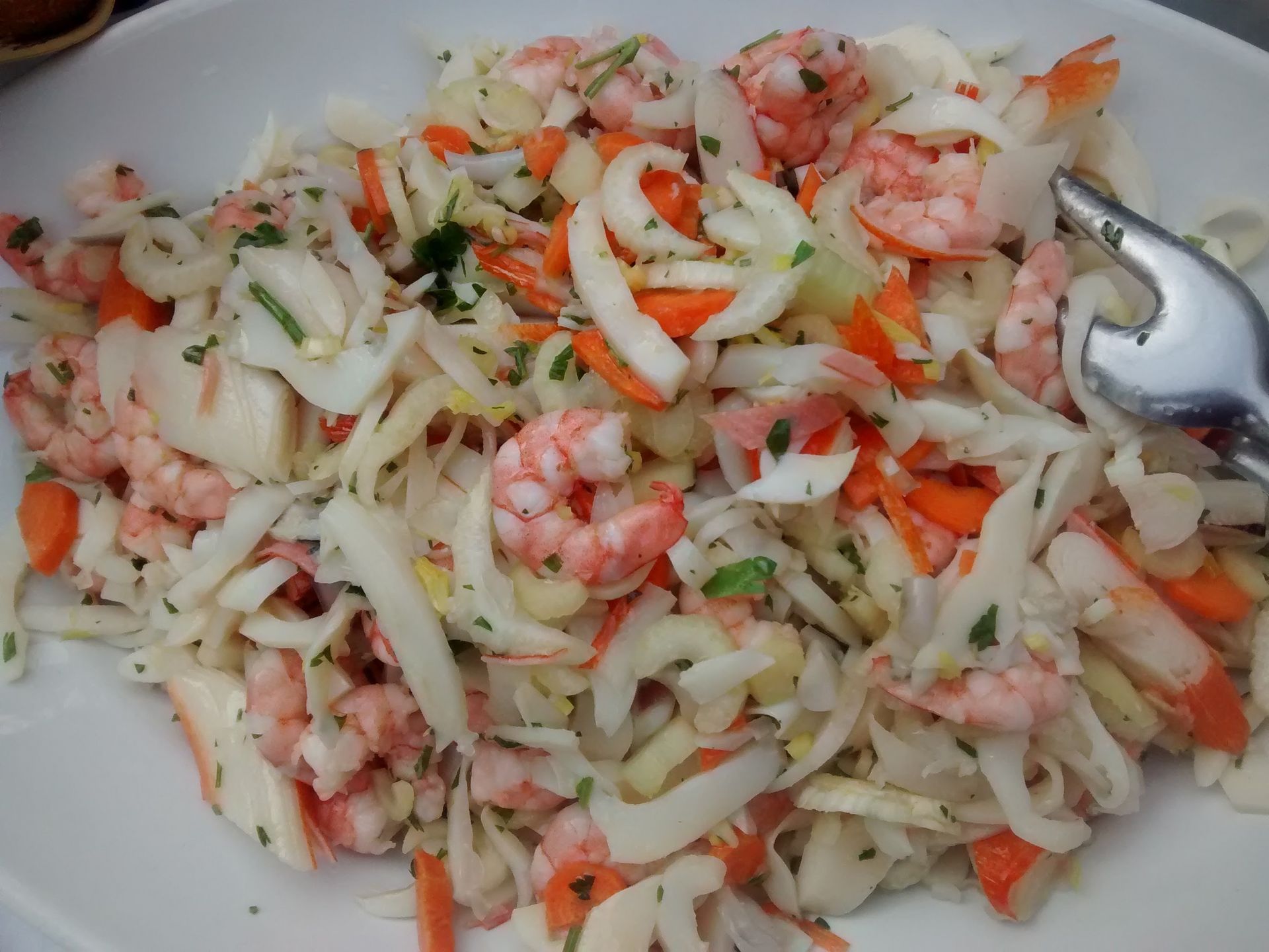 Insalata di gamberi e verdure con cavolo cappuccio e carote tagliate a julienne su un piatto bianco.
