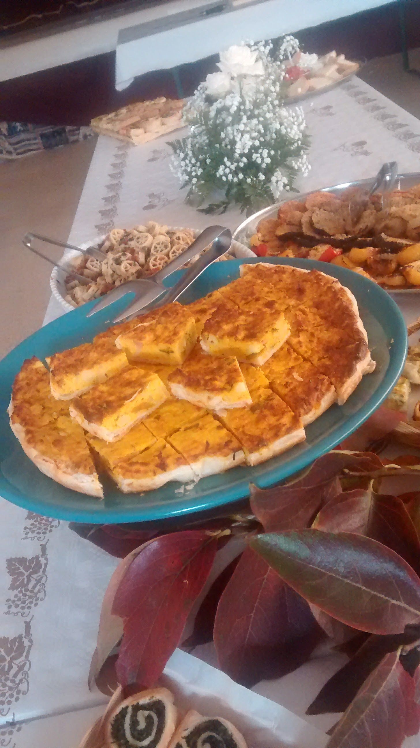 Tavolo con una frittata impiattata, contorno e fiori in un ambiente domestico.