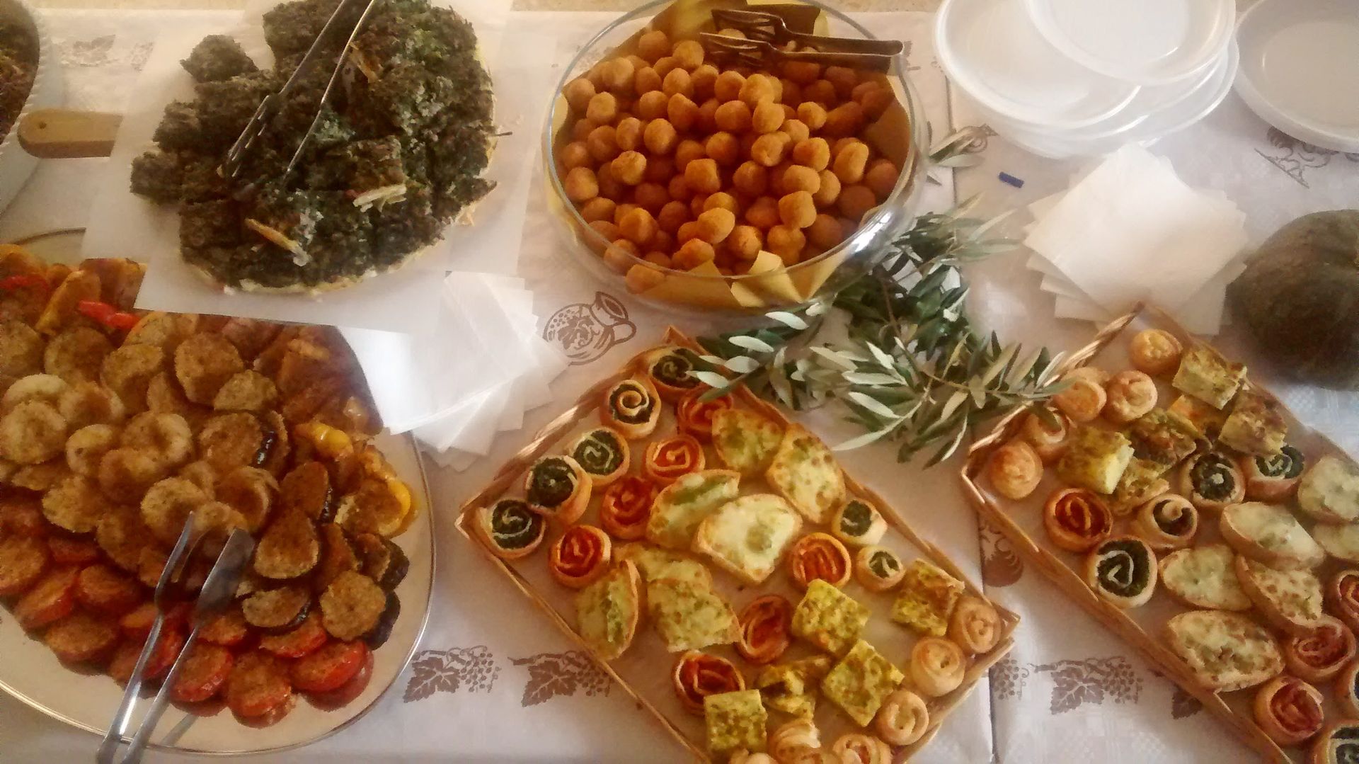 Antipasti assortiti e crostatine di frutta disposti su un tavolo con erbe aromatiche e tovaglioli.