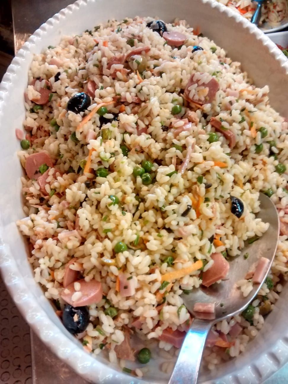 Ciotola di insalata mista di cereali con verdure a dadini, erbe aromatiche, olive nere e cucchiaio da portata.
