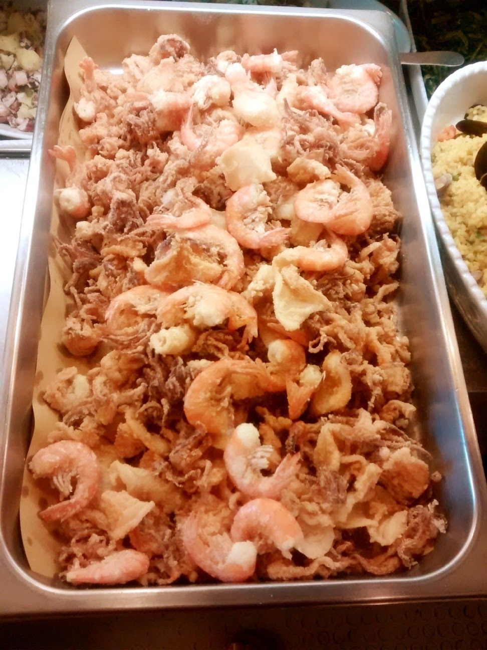 Vassoio di gamberi cotti a buffet, con una ciotola di riso parzialmente visibile di lato.