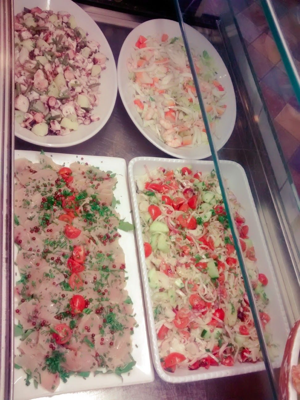 Quattro vassoi di verdure ed erbe aromatiche colorate tritate per insalata in una vetrina da gastronomia.