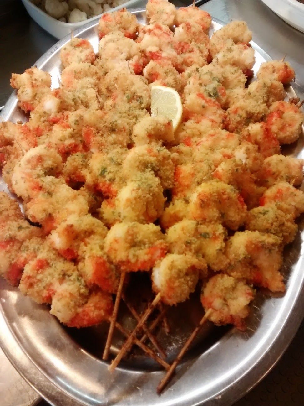 Vassoio di stuzzichini impanati e fritti, infilzati su spiedini e conditi con spezie rosse e uno spicchio di limone.