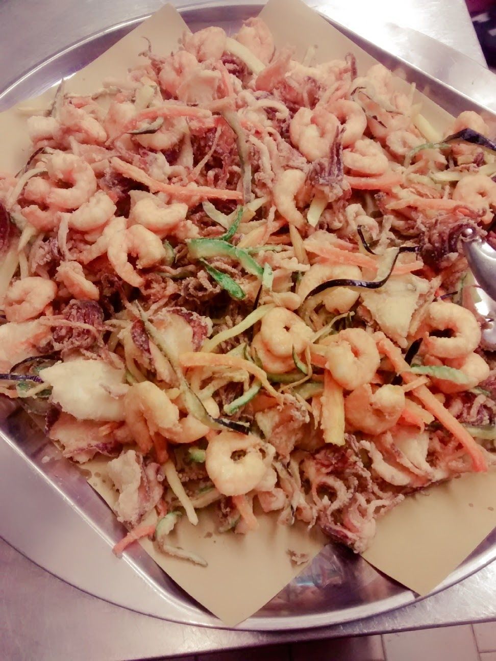 Vassoio di frutti di mare e verdure fritte con spicchi di limone, guarnito con erbe aromatiche.