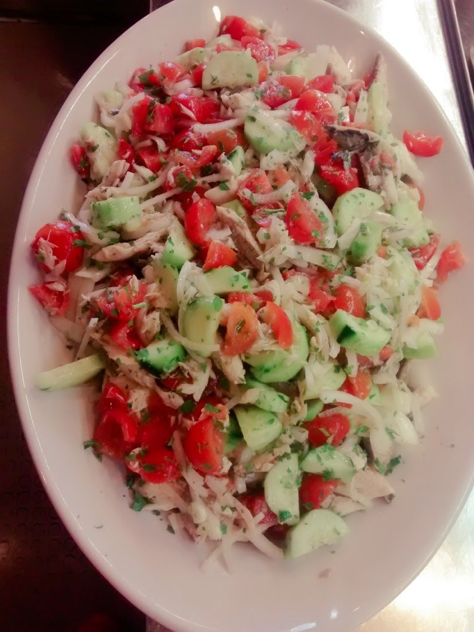 Insalata mista con cetrioli, pomodori, cipolle ed erbe aromatiche tritate, servita su un piatto bianco.