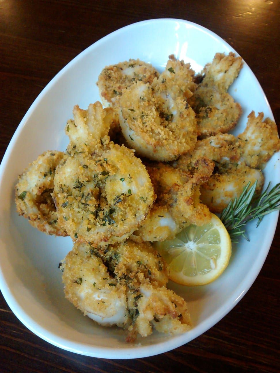 Gamberi fritti impanati con spicchio di limone ed erbe aromatiche in una ciotola bianca.