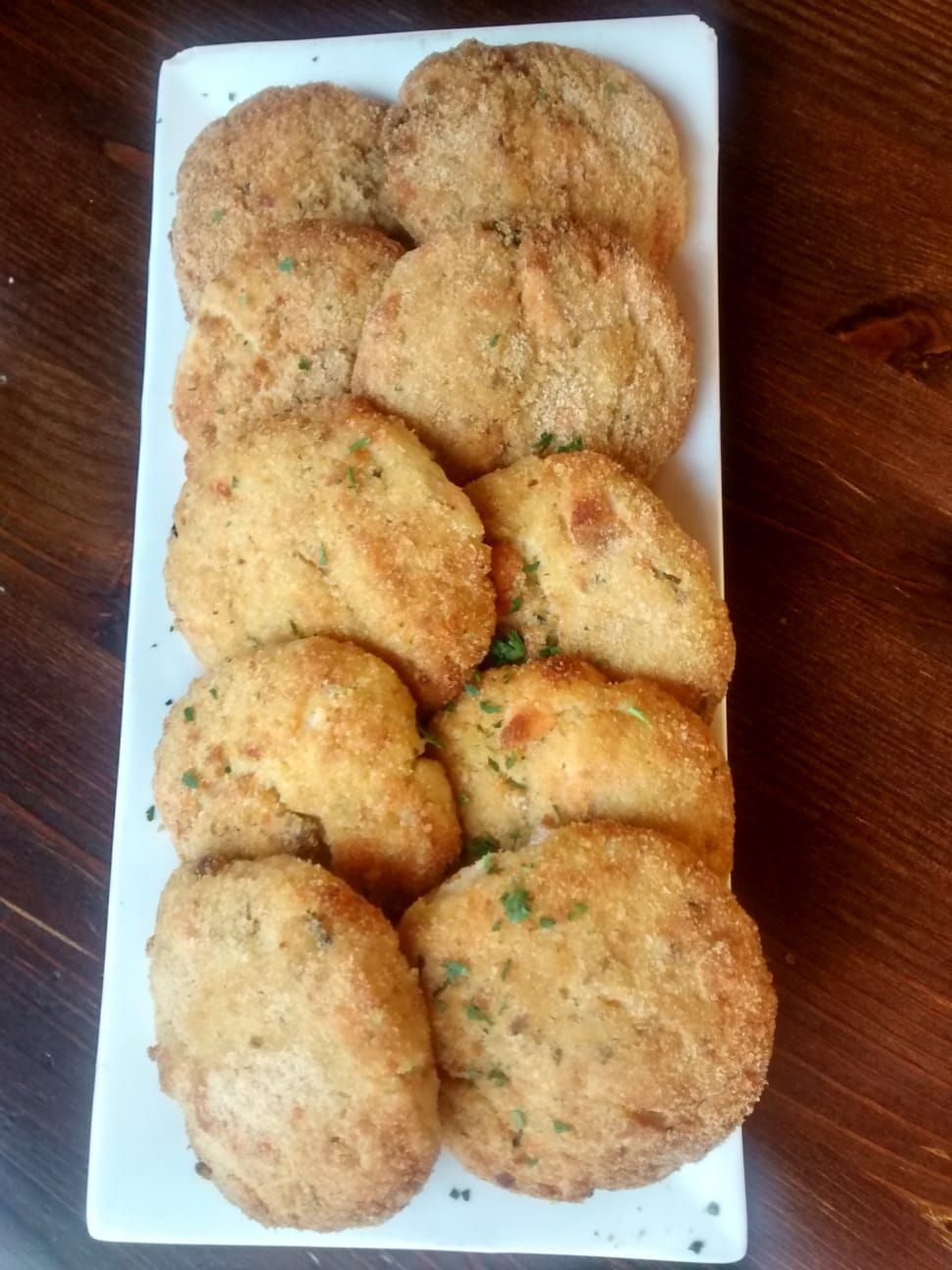 Piatto di frittelle dorate disposte in file su un piatto rettangolare bianco.