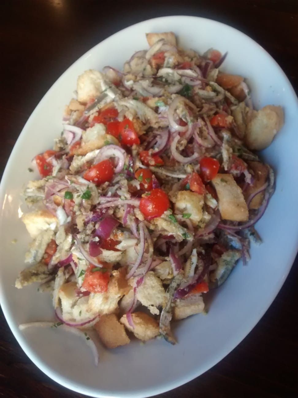 Insalata mista con cipolle rosse, pomodori e patate su un piatto bianco.
