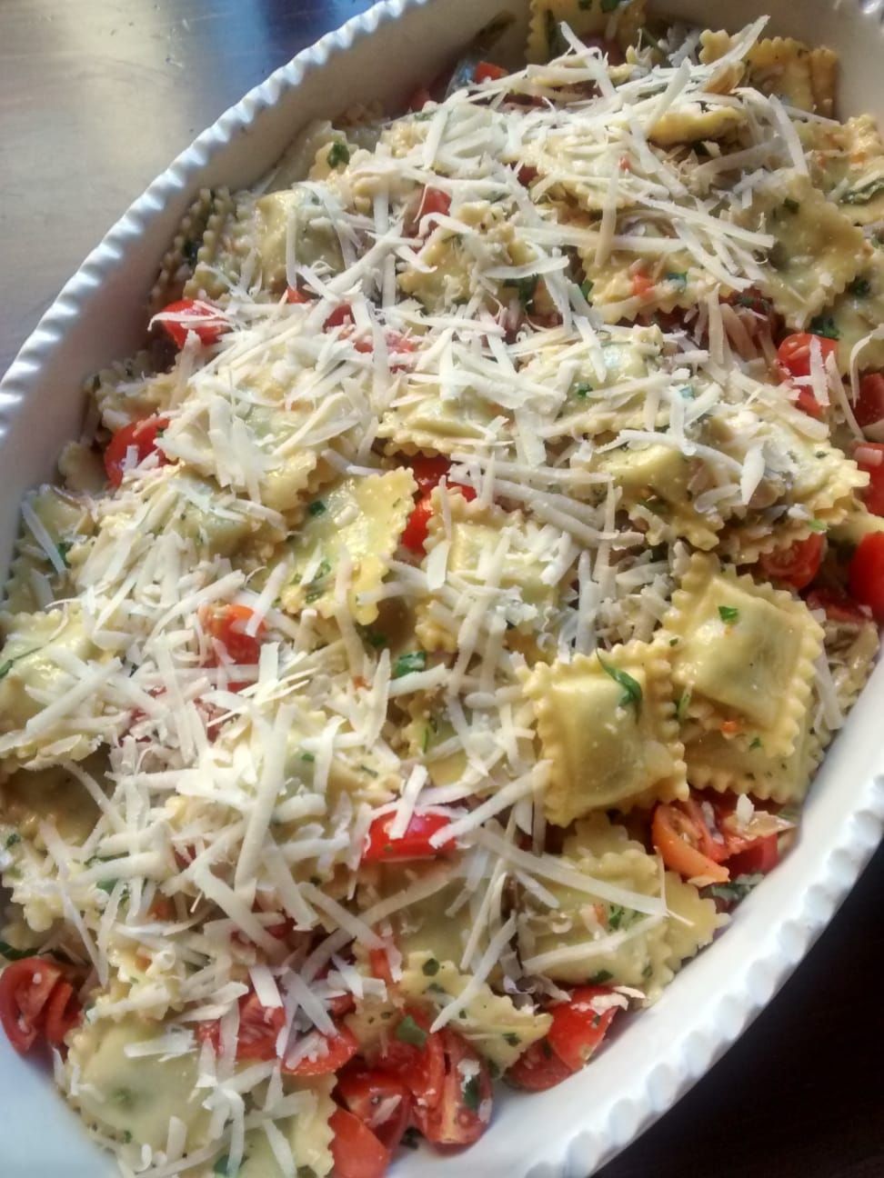Piatto di ravioli conditi con formaggio grattugiato e pezzetti di pomodoro rosso