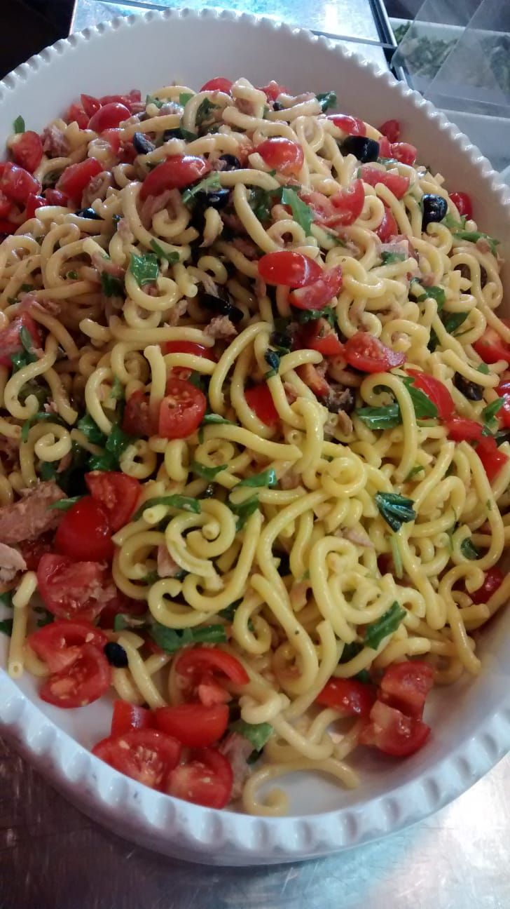 Vassoio di spaghetti conditi con pomodorini, erbe aromatiche e pezzetti di condimento rosso.
