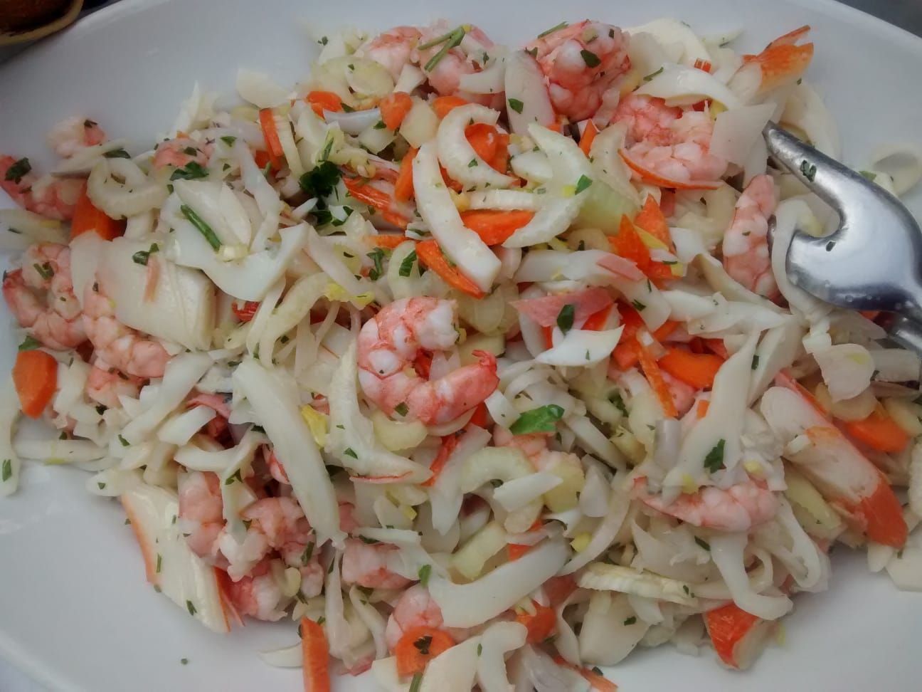 Insalata di gamberi con cavolo cappuccio, carote e cetrioli tagliati a julienne in una ciotola bianca.