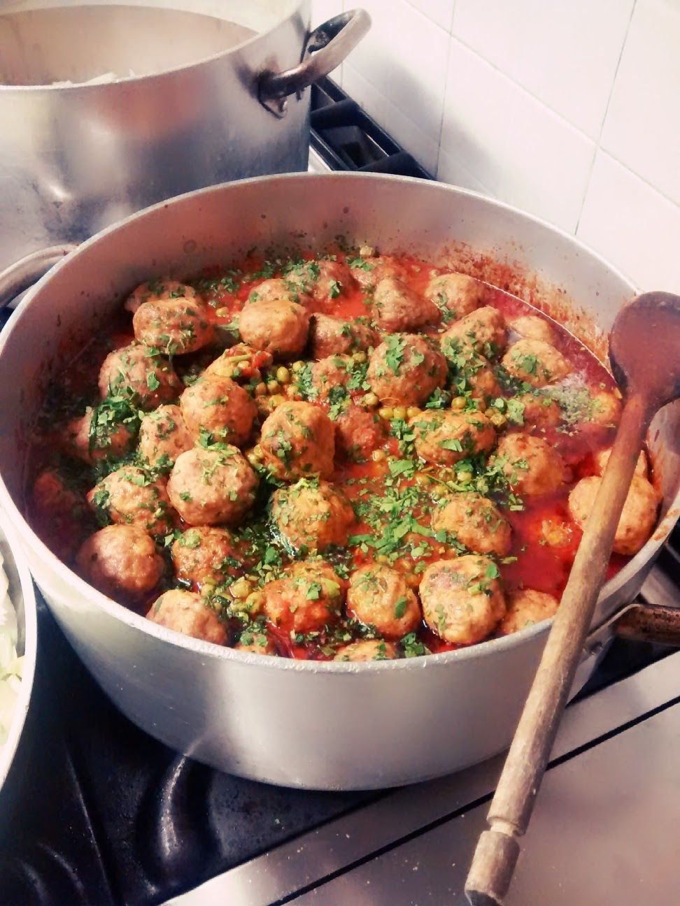 Pentola di polpette in salsa di pomodoro con erbe aromatiche, servita con un cucchiaio di legno sul fornello.