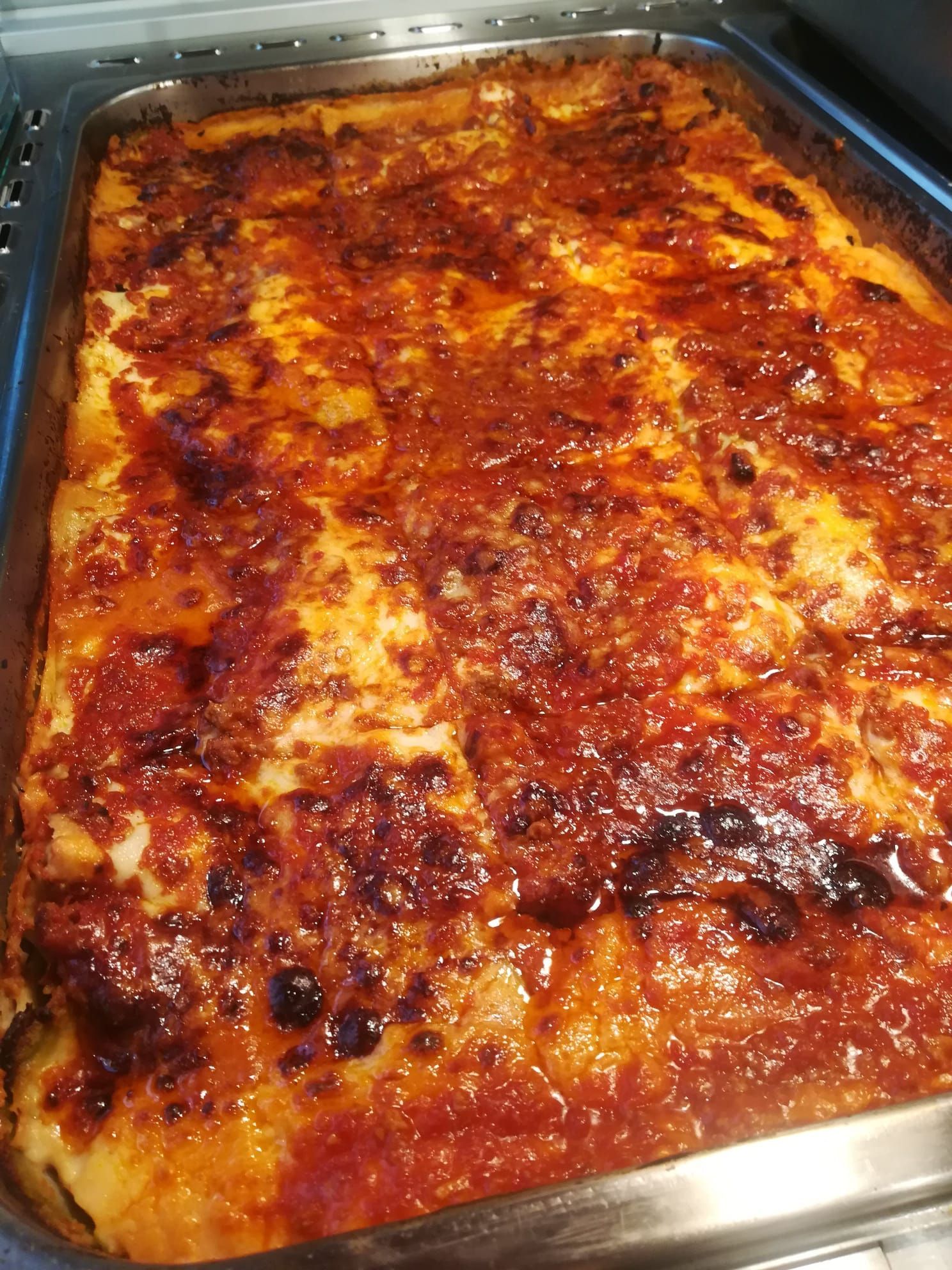 Pasta al forno in una teglia di acciaio inox, ricoperta di formaggio fuso e salsa di pomodoro.