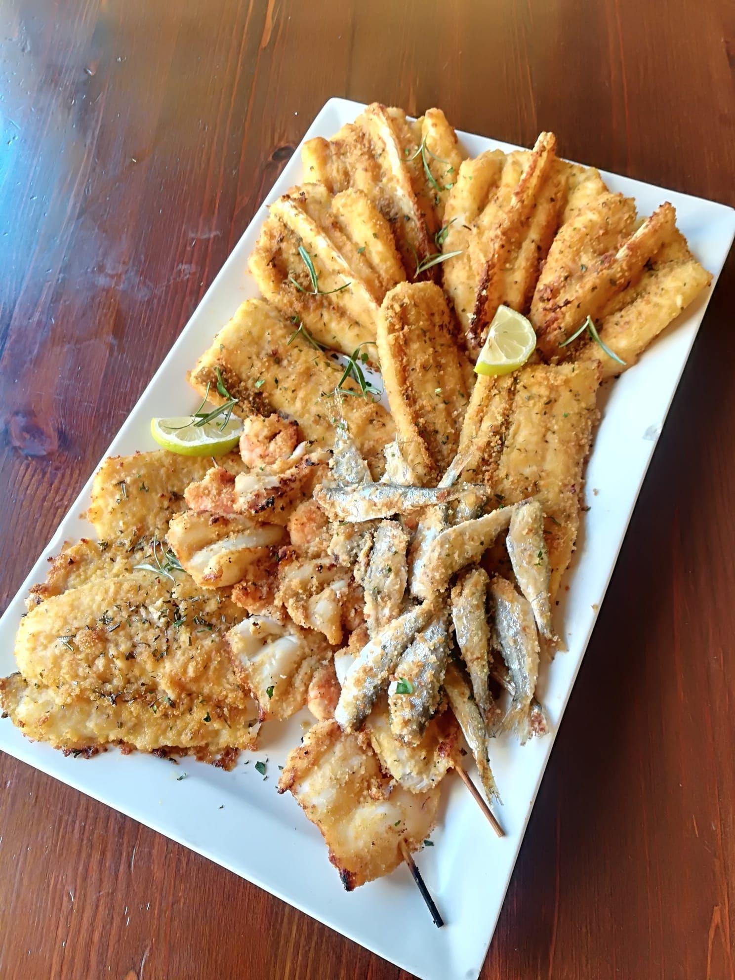Piatto di frutti di mare e filetti di pesce fritti assortiti su un vassoio bianco con spicchi di limone su un tavolo di legno.