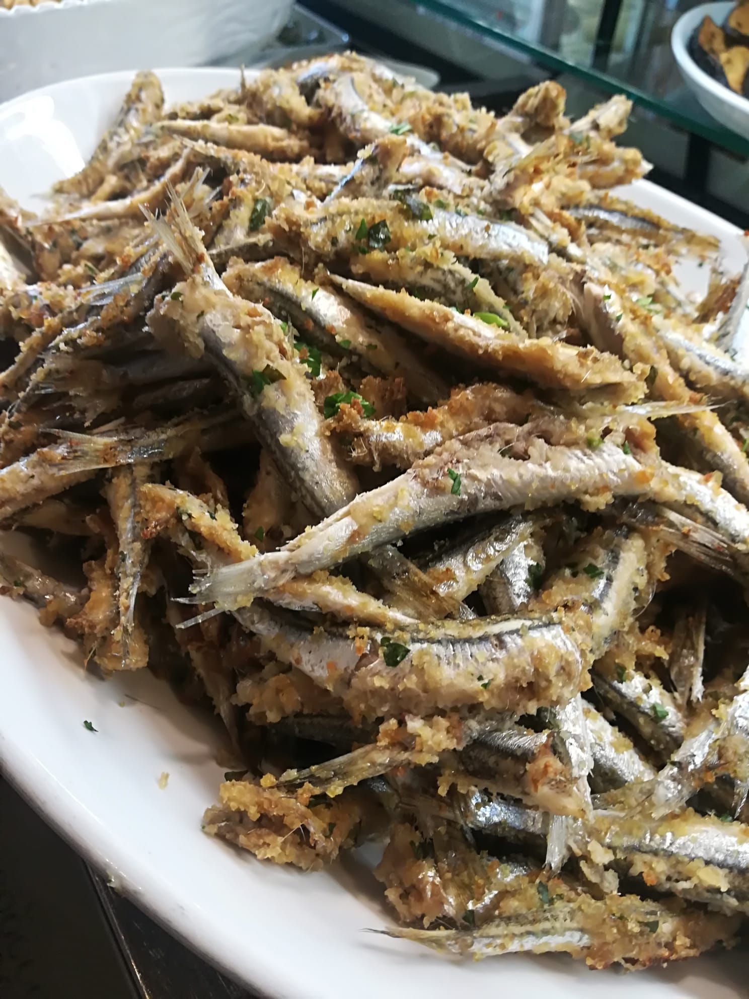 Piatto di pesciolini fritti, dorati e croccanti, impilati su un piatto bianco.