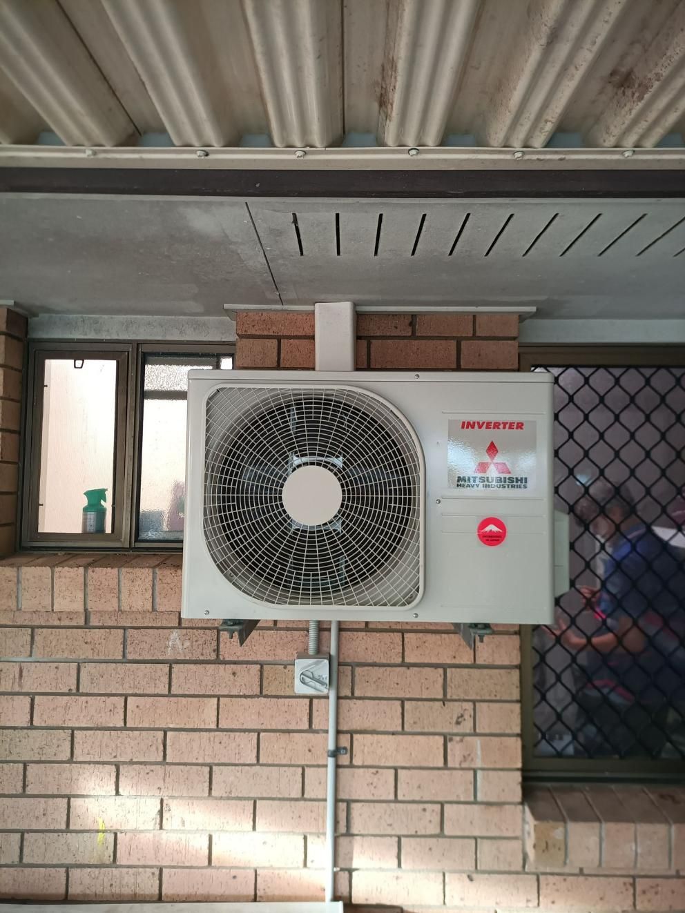 An Air Conditioner is Mounted on a Brick Wall Next to a Window — Instant Spark Electrical in Glen Isla, QLD