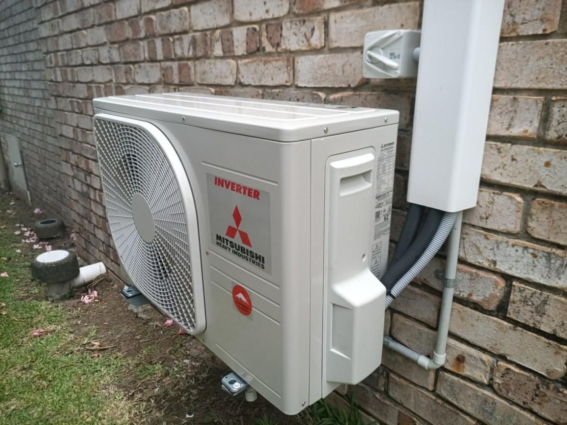 A White Air Conditioner is Mounted on a Brick Wall — Instant Spark Electrical in Glen Isla, QLD