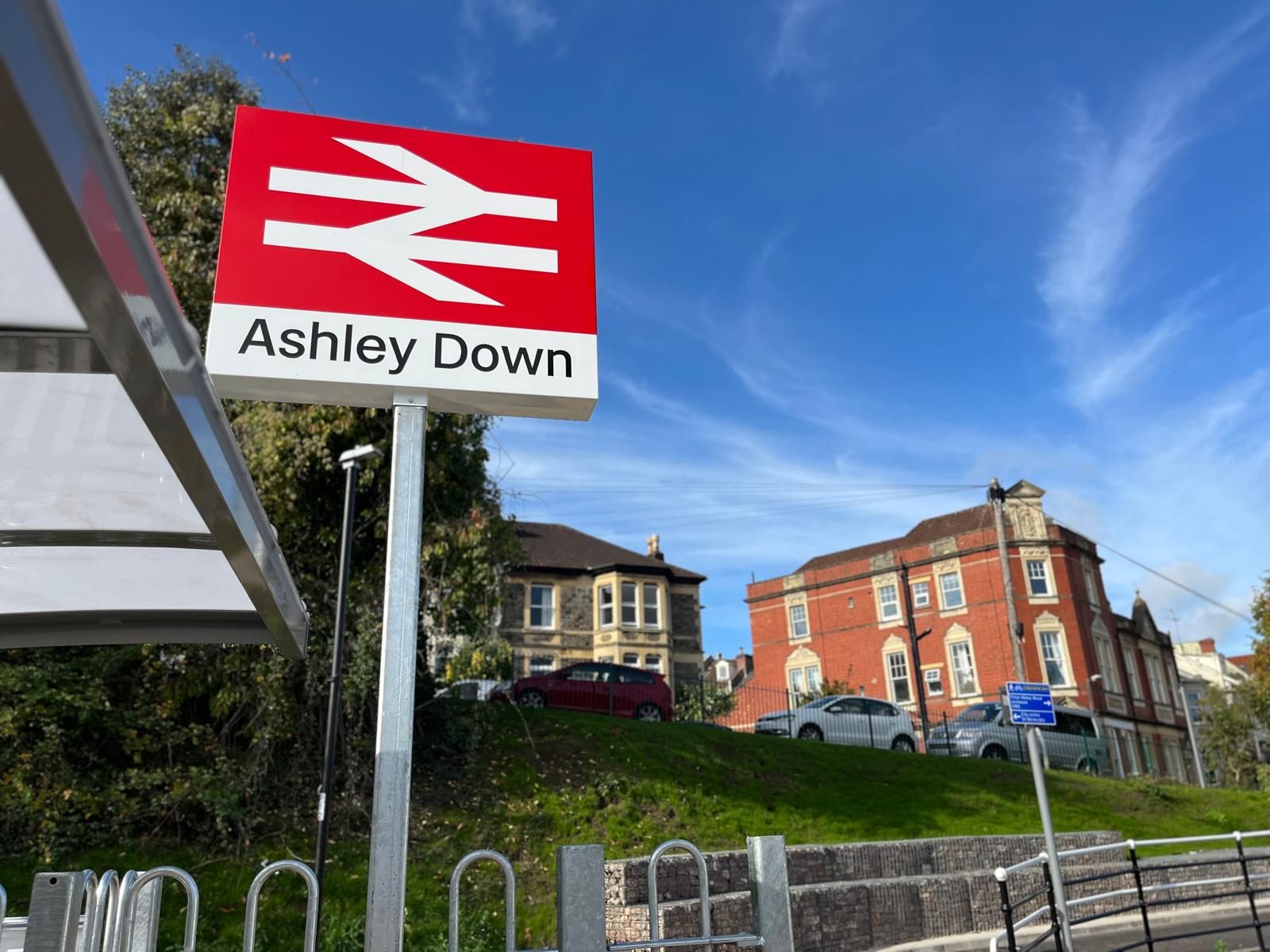 Ashley Down railway station sign with buildings and blue sky in background.