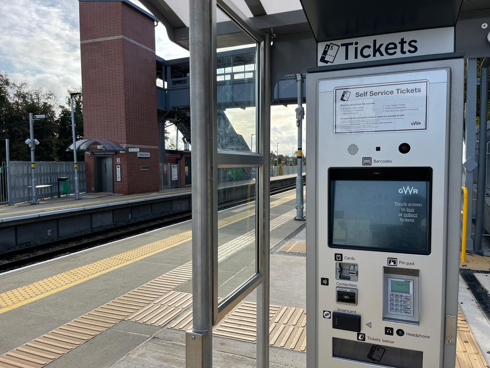 Train station platform with ticket machine, shelter, and brick building.