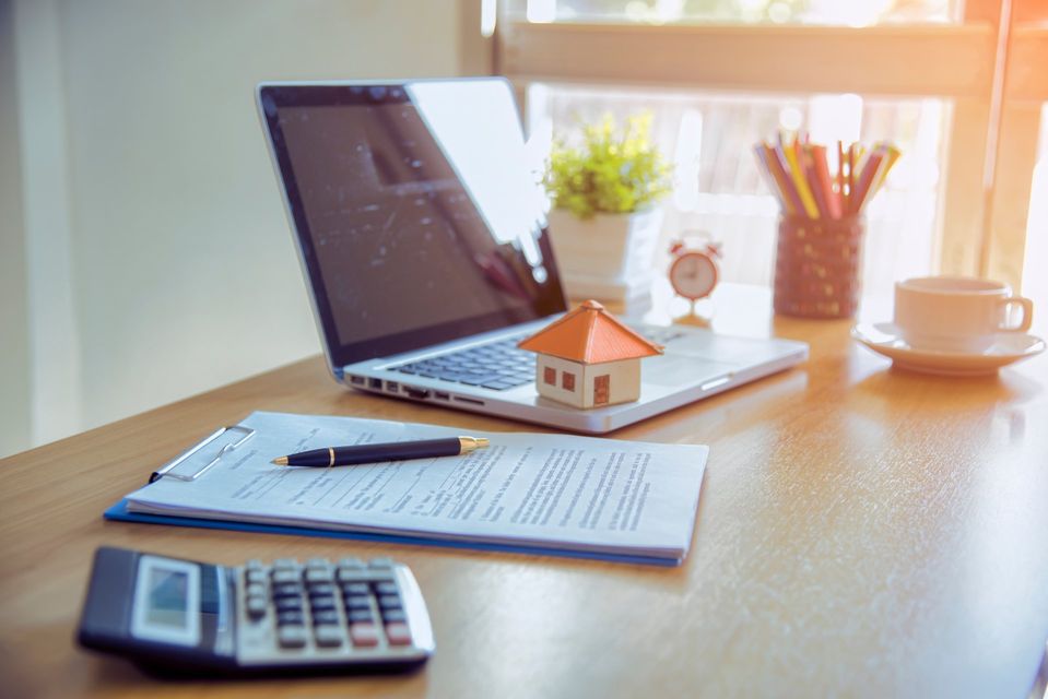 A desk with a laptop , calculator , pen , and a model house.