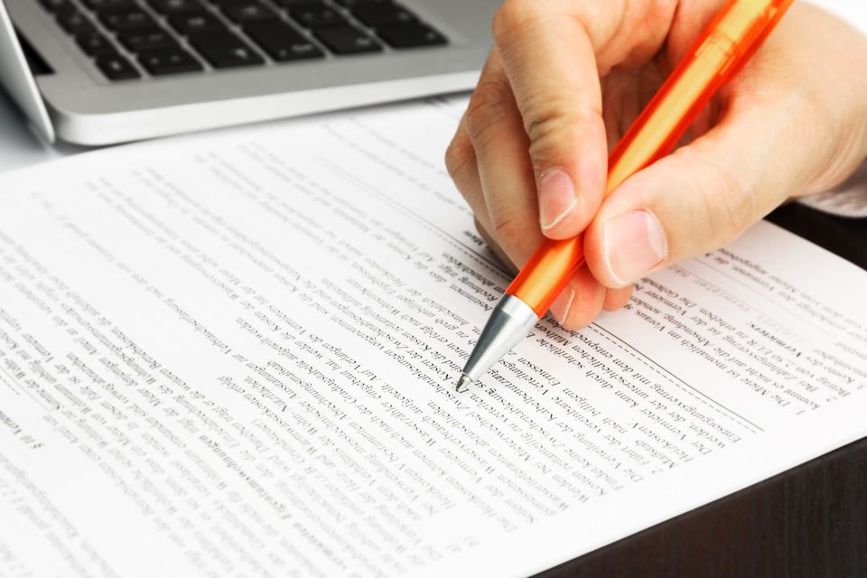 A person is writing on a piece of paper with an orange pencil