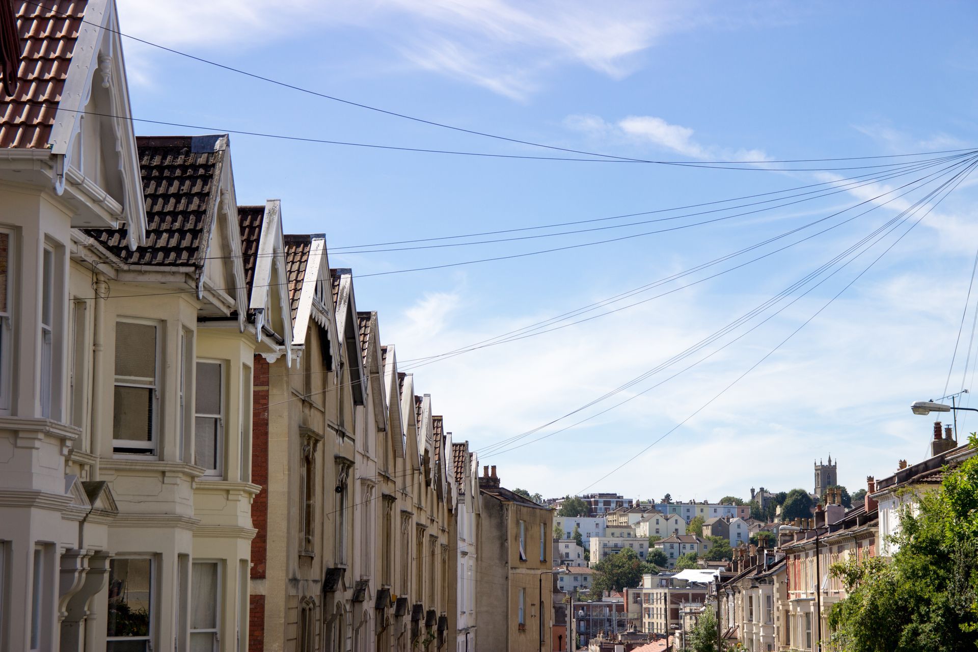 A row of houses on a hillside with telephone wires hanging from the roofs.