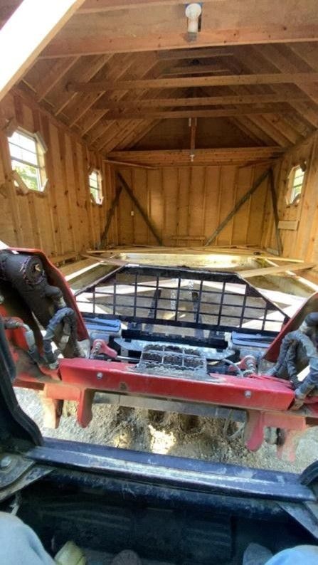Red ATV parked inside a wooden shed with open rear doors and sunlit windows.
