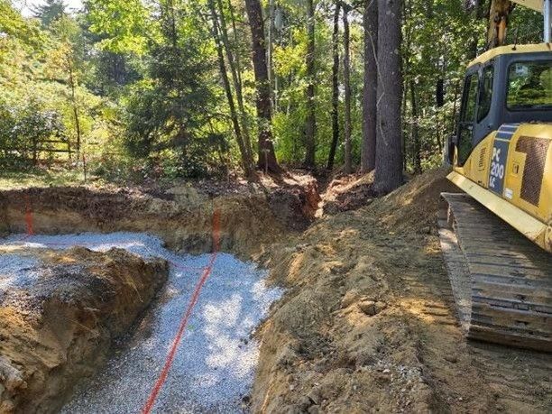 Yellow construction excavator beside a dirt trench in a wooded area