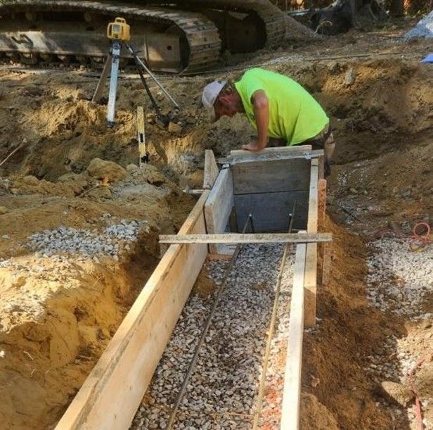 Worker in neon vest aligning a concrete form trench with survey equipment at a construction site