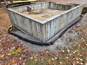 Weathered concrete planter bed with black edging on a leaf-strewn ground.