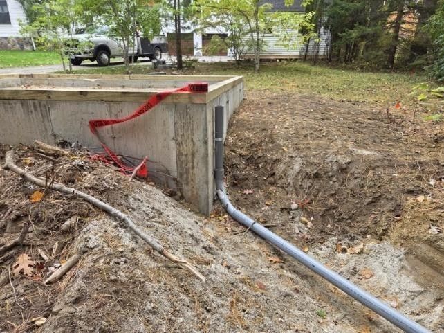Red ribbon tied around a concrete drainage culvert in a dirt yard with a pipe opening.