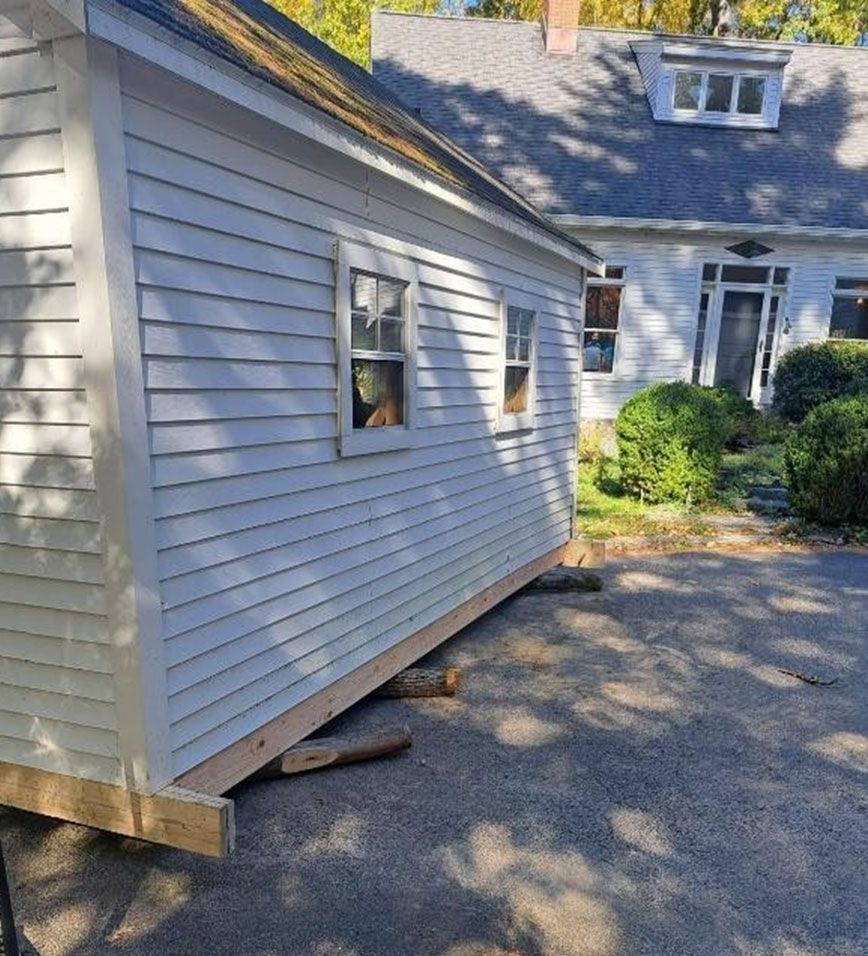 Detached garage wall visibly leaning outward onto a driveway, with white siding and a house in the background.