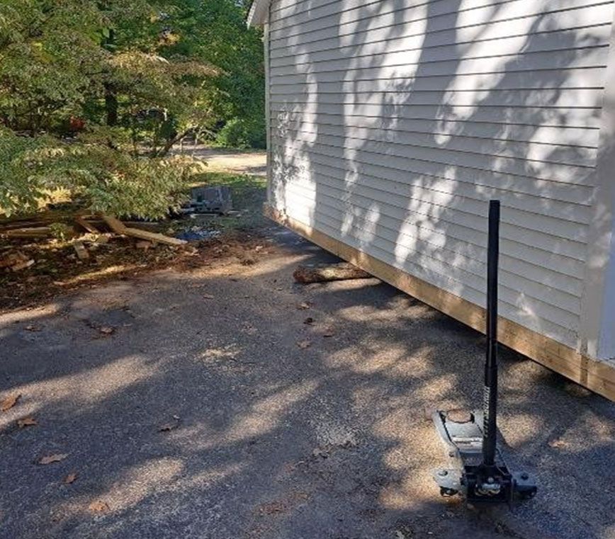 Driveway beside a white house, with a black post hole digger standing on the pavement.