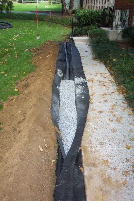 Backyard walkway under construction, with black landscape fabric and gravel beside a concrete path