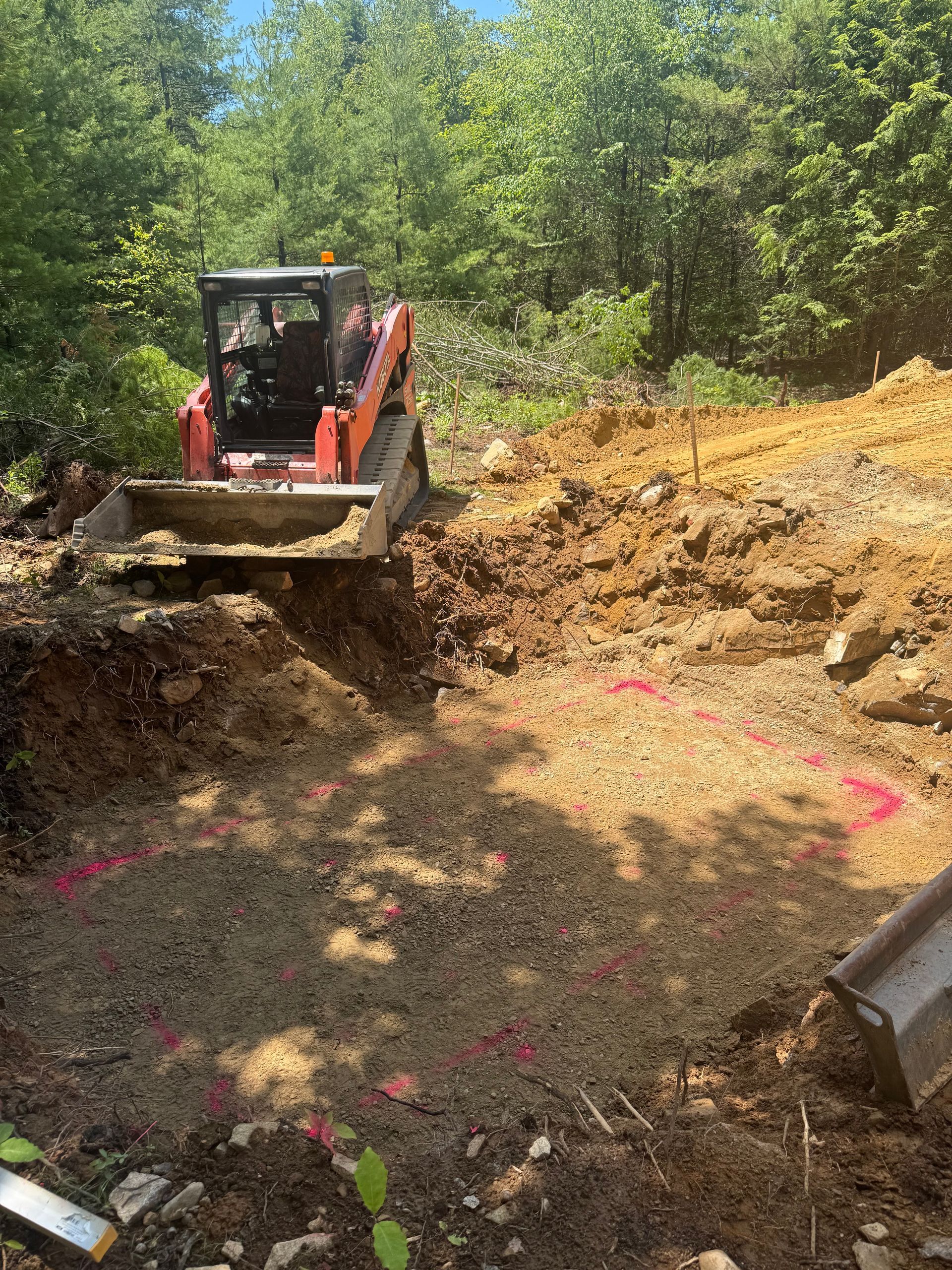 Small orange bulldozer clearing dirt on a wooded hillside excavation site