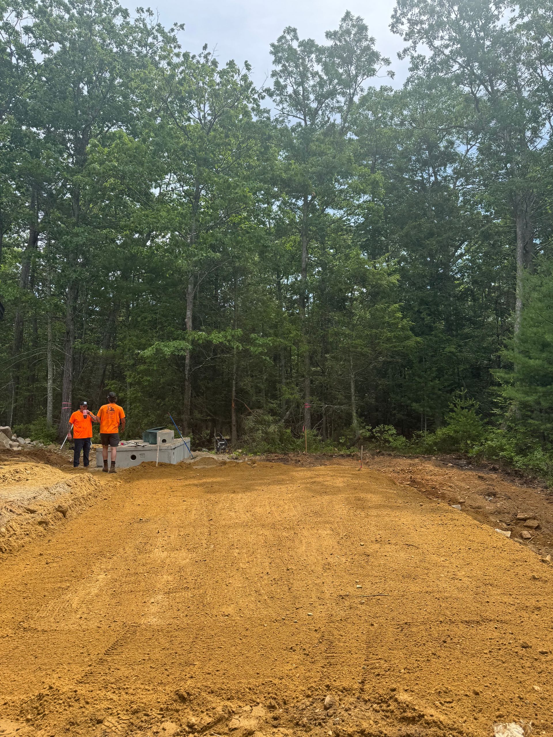 Two men are walking through a dirt field in the woods.