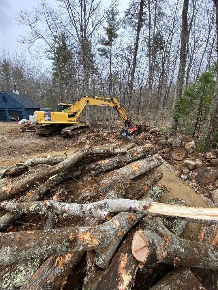 A pile of logs with a yellow excavator in the background.
