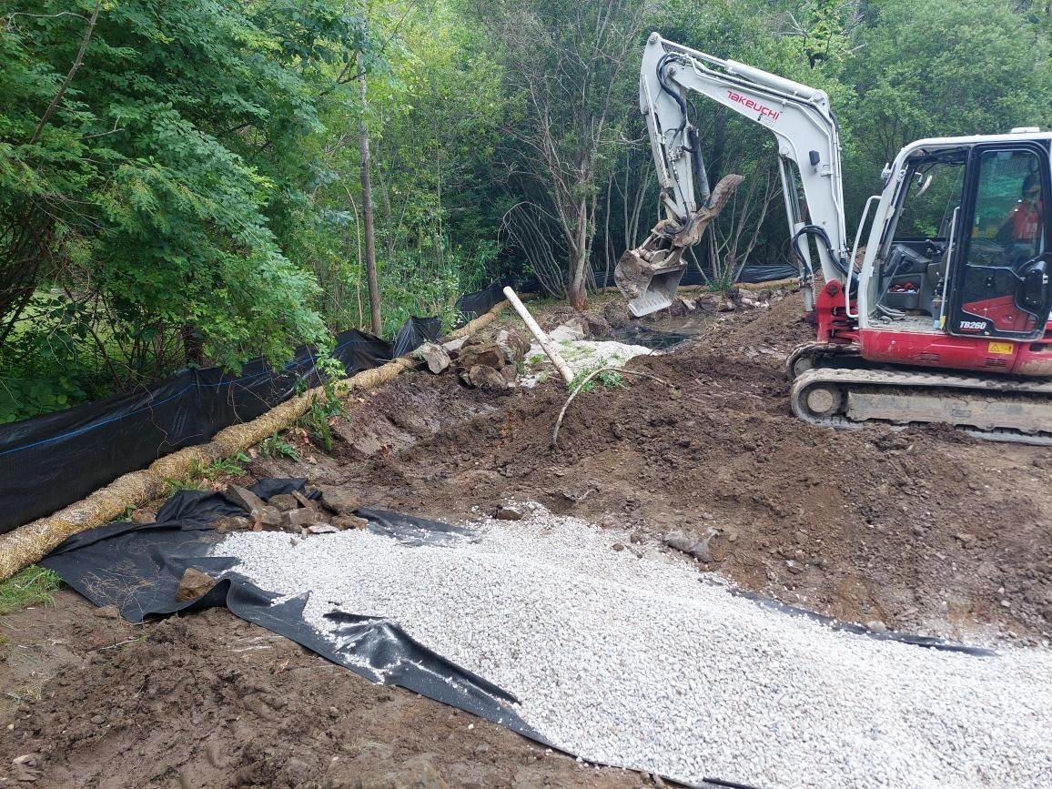Excavator clearing a muddy landslide beside a gravel path in a wooded area