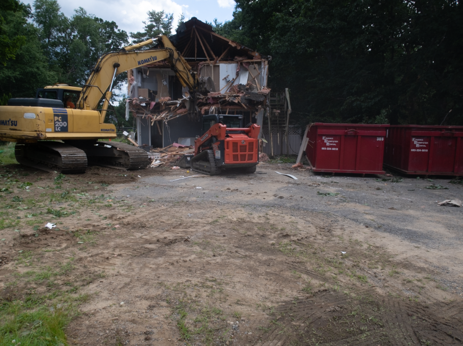 A large yellow excavator is demolishing a house.