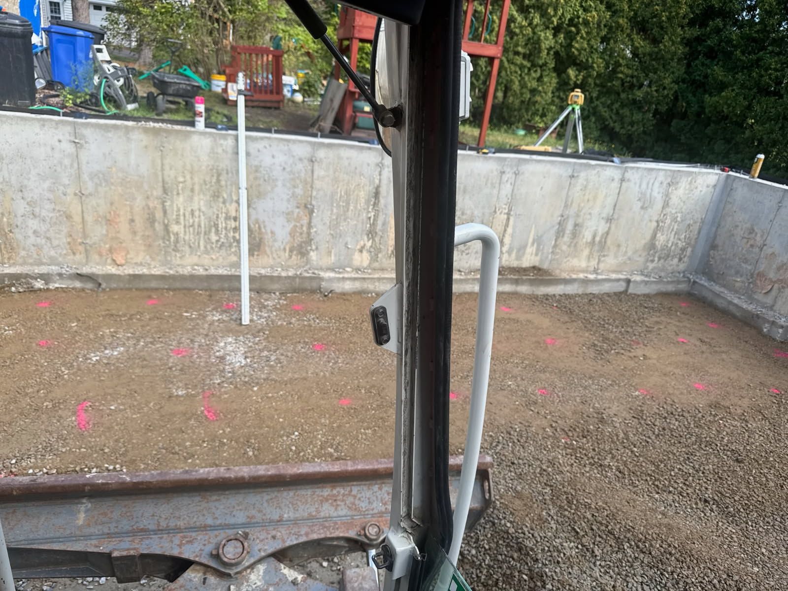 Rain-speckled ground beside a concrete wall, viewed through a vehicle window and black pillar.