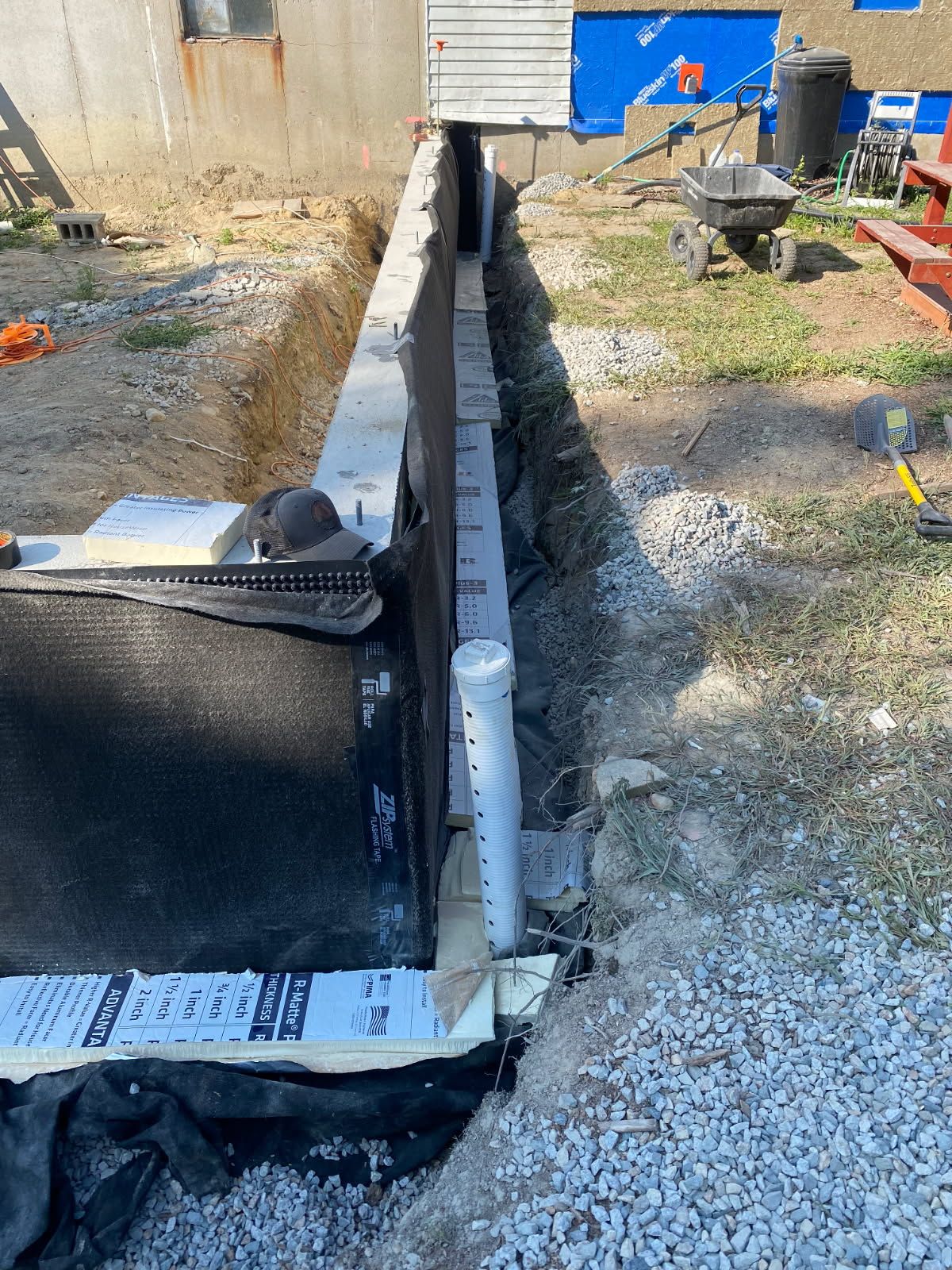 Construction site trench with a white pipe running through gravel beside a black barrier and blue container.