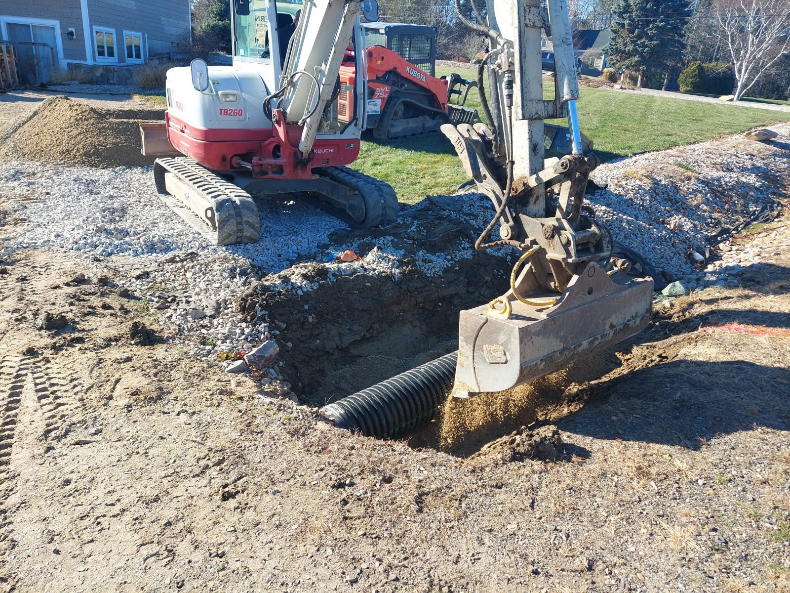 Excavator digging a trench in a gravel worksite near a house