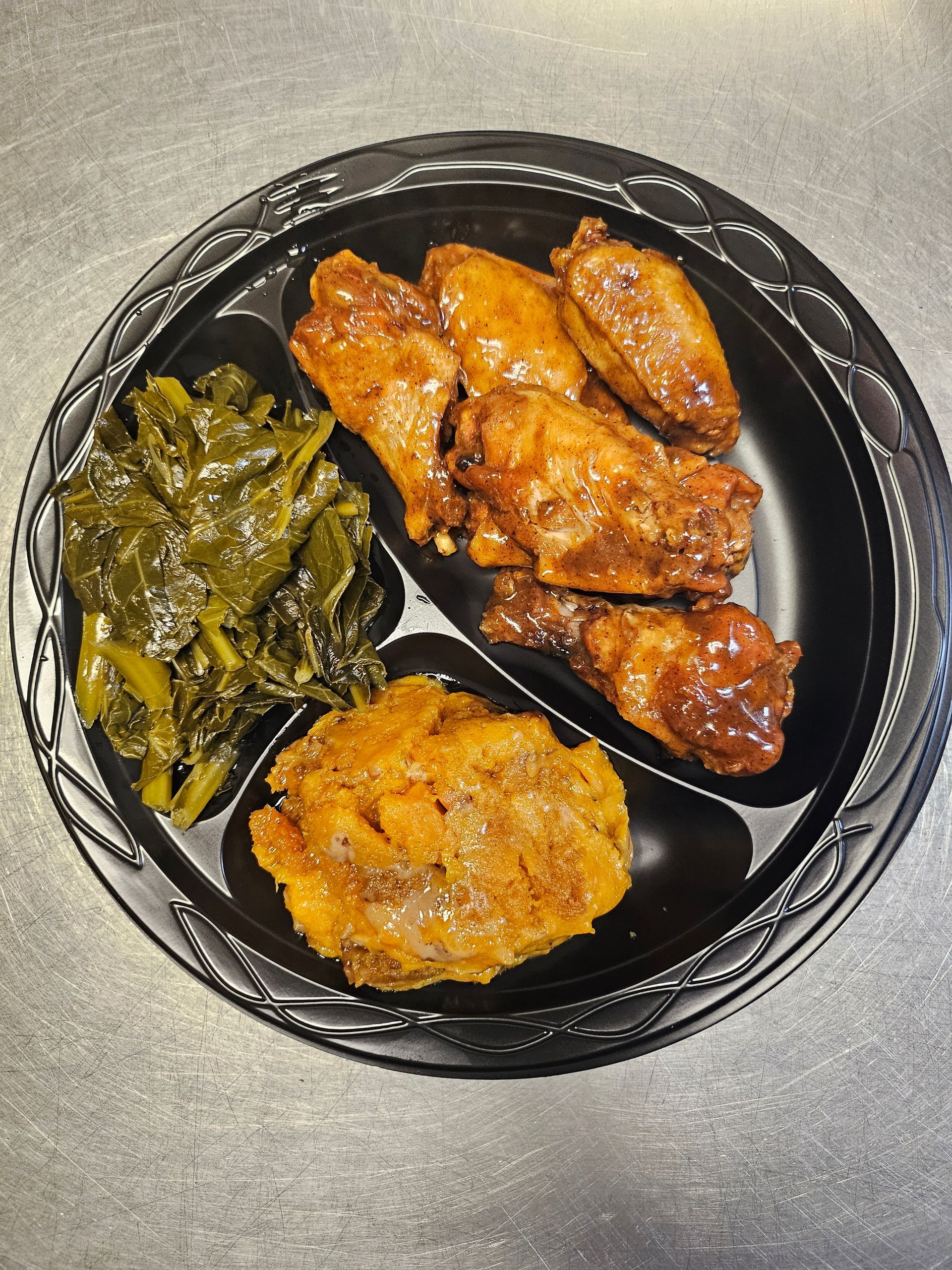 A plate of food with chicken wings , mashed potatoes and greens on a table.