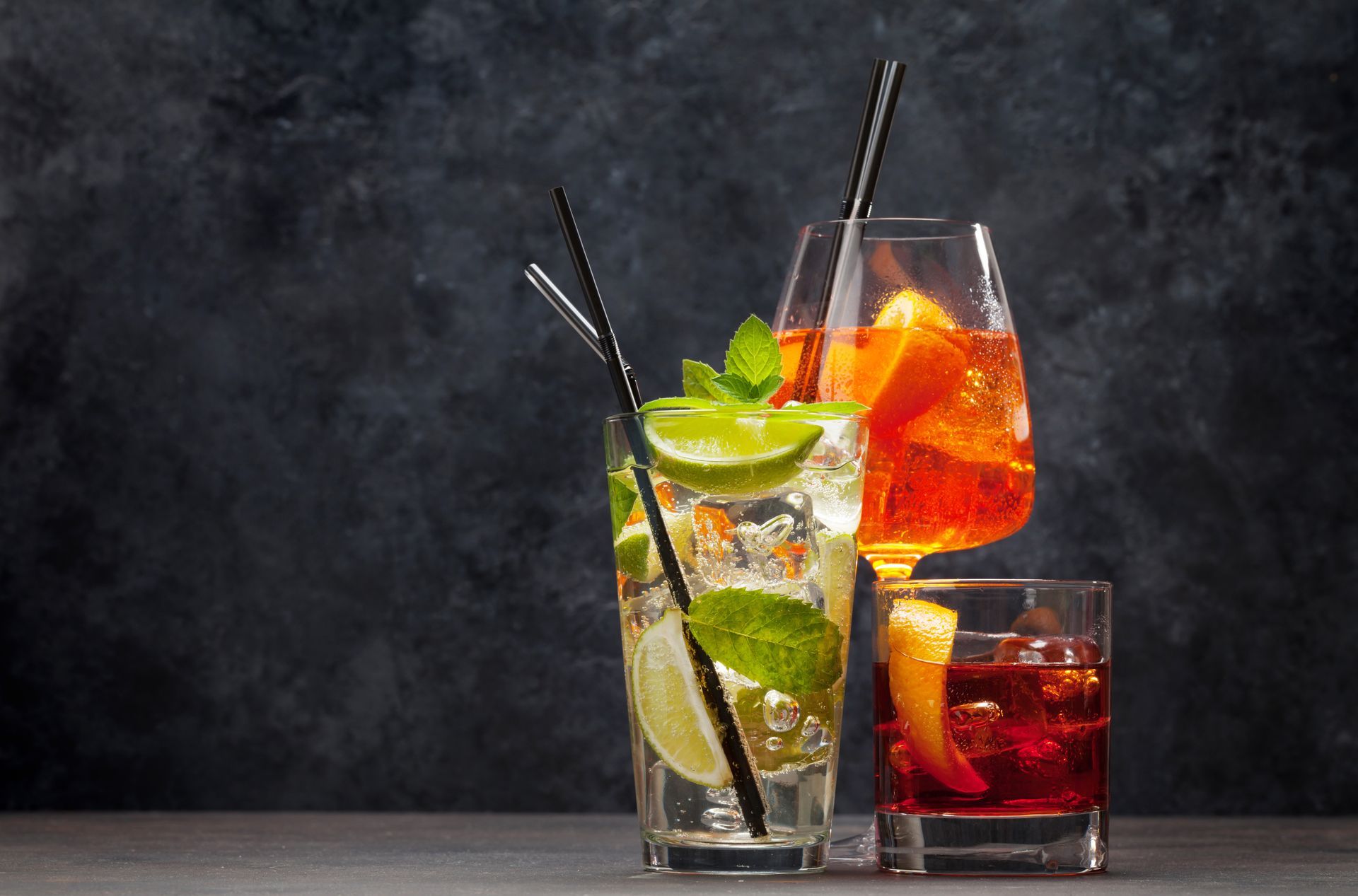 Three different types of cocktails in glasses with straws on a table.